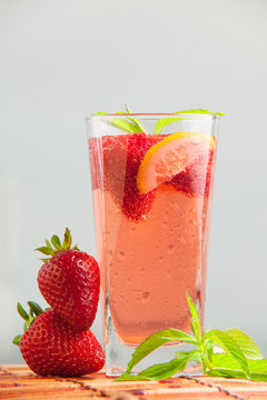 Glass of strawberry lemonade with pieces of strawberry, lemon and fresh mint. Closeup of mojito with beach on background. Fresh summer bright strawberry cocktail.