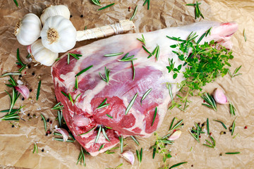 Raw lamb leg on crumpled paper background with herbs