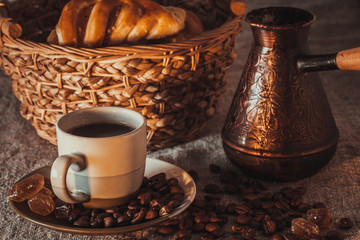 cup of coffee on textile with beans, dark candy sugar, pots, basket and cake