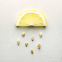 Sour rain / Creative concept photo of a lemon slice with seeds falling down on grey background.