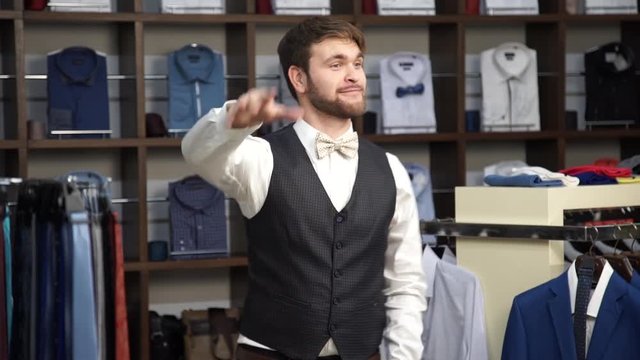 Young attractive man with a beard, dressed in a business suit, dancing in a men's clothing store.