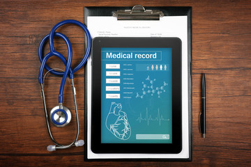 Medical record on tablet screen with stethoscope on wooden background