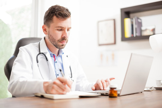 Young doctor taking notes and using a laptop