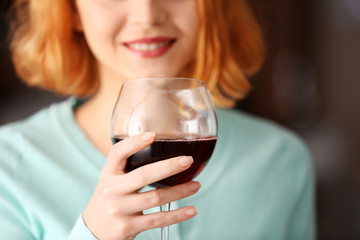 Young woman with glass of red wine on light blurred background