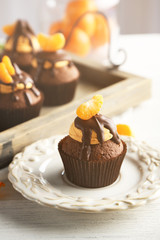 Tasty cupcakes with slice of mandarin and chocolate on a tray over light wooden background