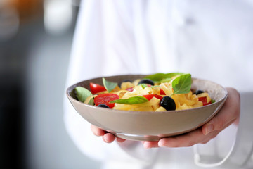 Chef hands holding delicious cold pasta salad in bowl closeup