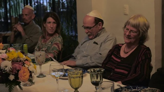 A man reads from a book at a dinner table during a passover seder