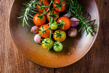 Cherry tomatoes, garlic and rosemary in ceramic plate