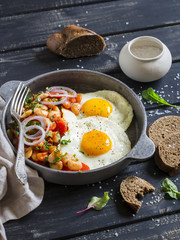 Fried egg, beans in tomato sauce with onions and carrots, fresh cucumbers and tomatoes, homemade rye bread - delicious  breakfast or snack  on dark wooden background