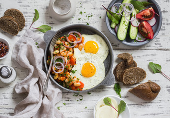 Delicious  breakfast or snack - a fried egg, beans in tomato sauce with onions and carrots, fresh cucumbers and tomatoes, homemade rye bread on light wooden background