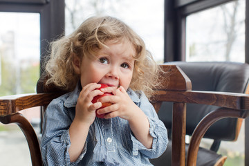 little child eating red apple indoors