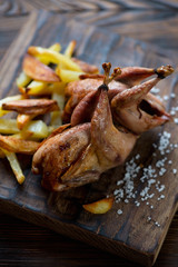 Closeup of whole baked quails and potato wedges, selective focus