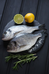 Stone slate with raw fresh dorado fish on a black wooden surface