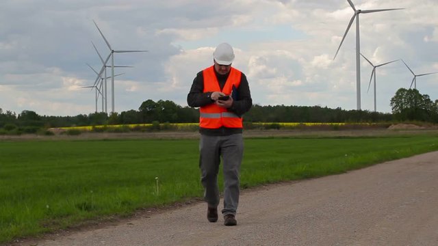Electrician engineer walking and take pictures on smart phone near Windmills
