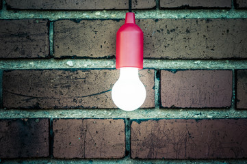 Gluehlampe vor Ziegelwand / Einzelne Gluehlampe vor alter Ziegelwand mit Textfreiraum.
