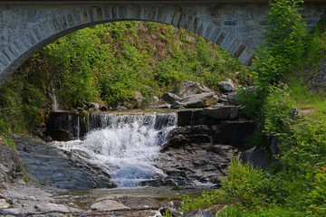 Old granite block arched bridge over a mountain river with whitewater