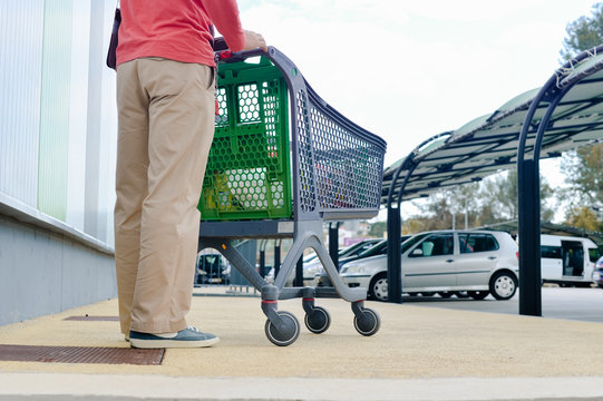 Person pushing a shopping cart in car park, outdoors background