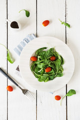 Rocket salad with cherry tomatoes on white wooden background