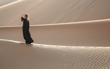 A woman in abaya in sand dunes in Liwa Desert, Abu Dhabi, UAE