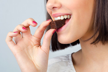 Portrait of the beautiful girl eating chocolate cookies isolated on gray