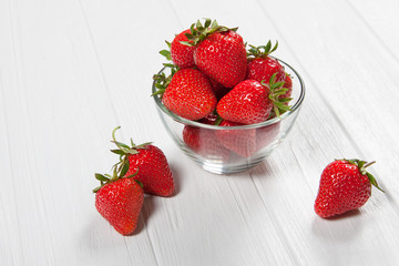Red fresh strawberry in a bowl on white wooden background
