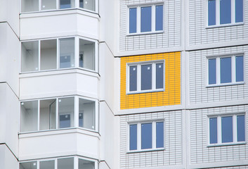 Новостройка. Балконы и желтая стеновая панель на фоне белых панелей фасада нового жилого дома
