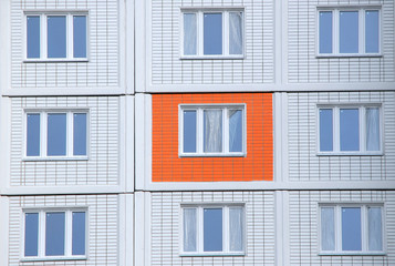 Fototapeta na wymiar Новостройка. Оранжевая стеновая панель на фоне белых панелей фасада нового жилого дома