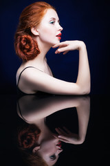 Naklejka premium Young woman with ginger hair over reflection mirror on blue back