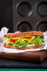 Toasted sandwich with salad leaves, tomatoes and cheese with fork on a cutting board on a dark background, closeup