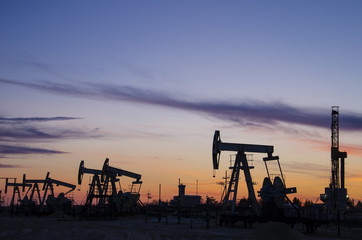 Pump jacks and derrick silhouette during sunset on the oilfield. Oil and gas concept.