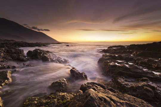 golden sunset at pacific ocean with waves on rocky shore - Powered by Adobe