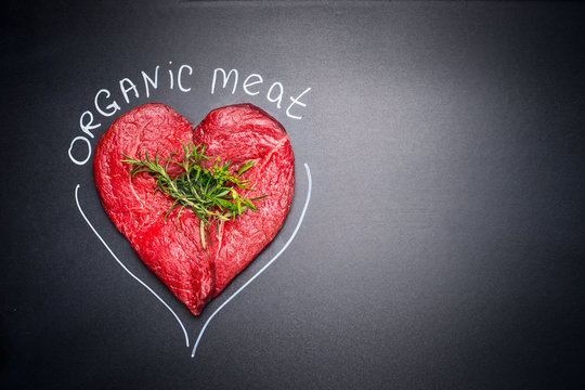Organic meat for healthy Eating. Heart shape raw meat with herbs and text on black blank chalkboard background, top view