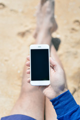 Person holding smartphone, beach background, closeup top view 