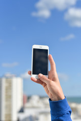 Hand holding mobile cell phone over city background. Closeup photo