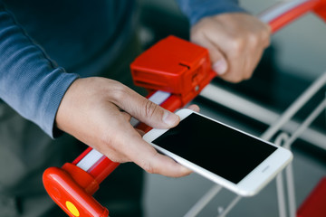 Person holding mobile phone in hand during shopping, closeup . Cart on background of store 