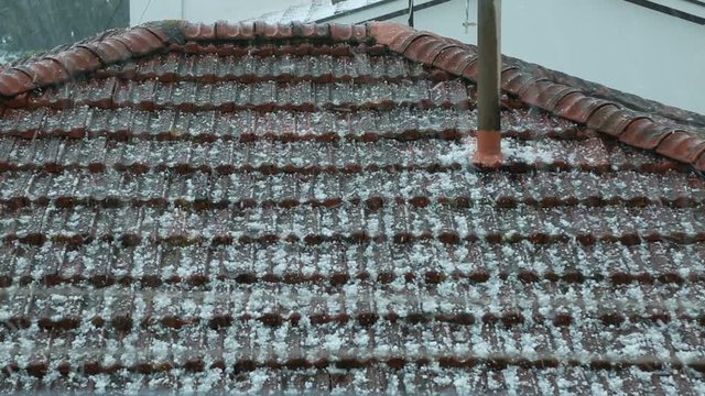 Hailstorm is Crashing onto the Roof of an House in a City.