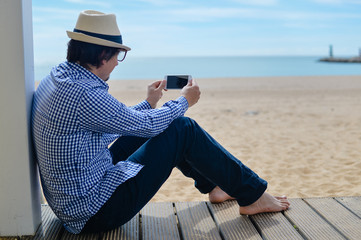 Person sitting using mobile smartphone, seaside background. back side view of barefoot man
