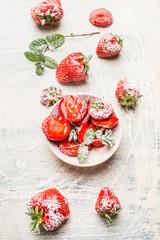 Bowl with sliced strawberries sprinkle with powdered sugar on white wooden background, top view