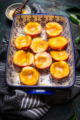 Baking dish with peaches  and honey on dark background, close up