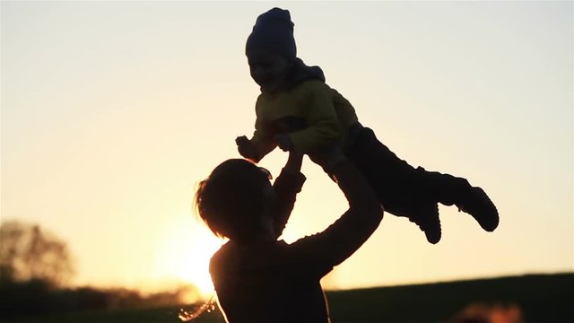 Young father throwing up son into air and catching him into hands at warm spring evening at golden hour in nature countryside backlit - family bond reunion fatherhood fathers day concept 