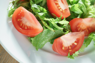 closeup photo of fresh summer salad with tomatoes, rucola and frillis leaves in plate on wood table, shallow focus