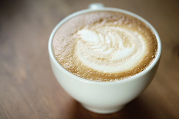fresh hot cup of coffe with latte art on wood table, shallow focus