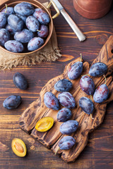 Fresh organic plums in copper bowl and on rustic wooden cutting board Top view