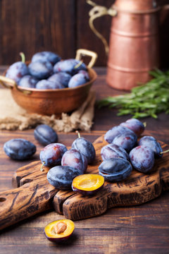 Fresh organic plums in copper bowl and on rustic wooden cutting board.