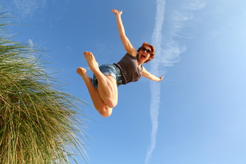 joy/ woman jumping for joy off a dune at the beach - obrazy, fototapety, plakaty