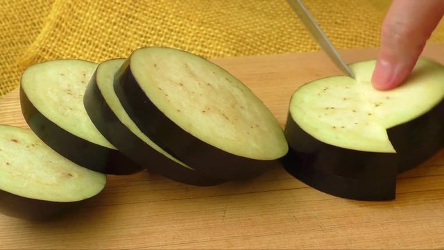 Female hands slicing eggplant vegetables on kitchen board close up 
