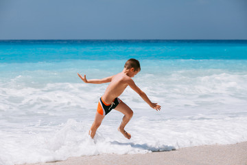 Beach vacation dream. Handsome young boy enjoying in beautiful tropical beach, running and playing with waves.