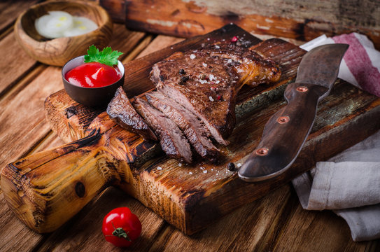 Sliced medium rare grilled Beef steak  with spices and ketchup  on cutting board on wooden background