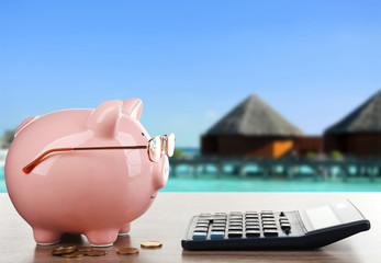 Pink piggy bank with glasses and calculator on resort background