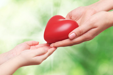 Heart in child and mother hands on green nature background. Concept of taking care, protection, helping and assistance
